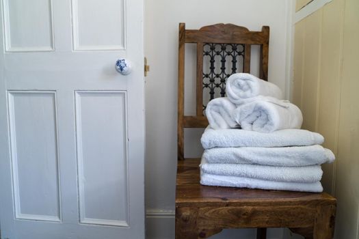an Hotel bathroom decor closeup. White towels,  on wooden stool and a door. Natural colors, still life. Studio shot