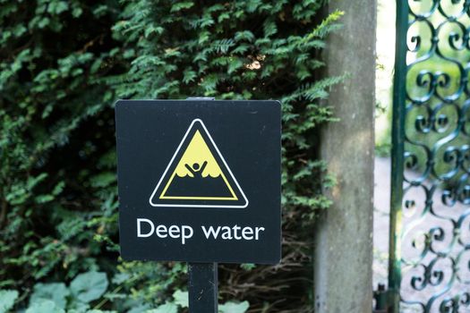 warning sign in black and yellow indicating the danger of drowning in deep water forbidding people to swim, english language