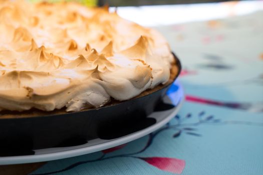 Cake with meringue frosting on a plate on a decorative set table outdoors close up