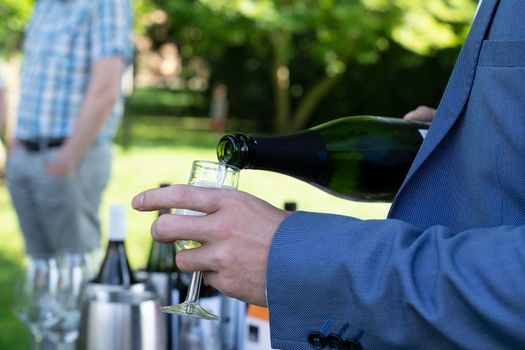 Male hands pooring white wine out of a bottle at an outdoor winetasting