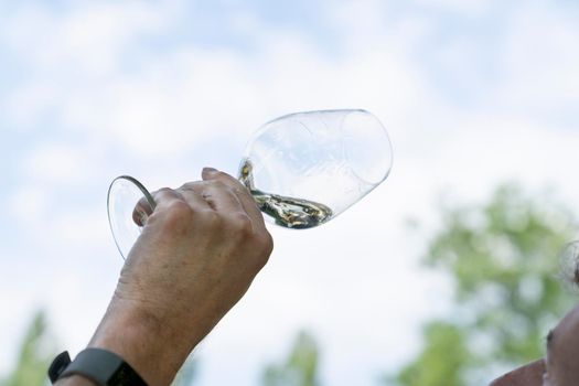 Male hands holding a glass of white wine at an outdoor wine tasting