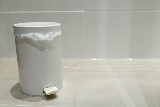 A closed white pedal bin standing on a tiled floor in a bathroom, concept for tidiness and the environment