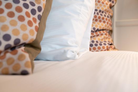 Red yellow and grey dotted scatter cushion and a white sleeping pillow on a fresh made bed in bedroom