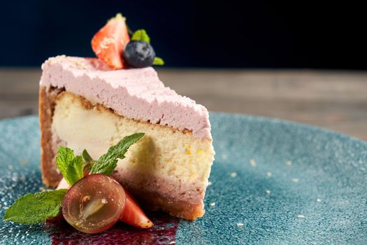 Close up of classic, traditional cheesecake served with blueberries and cranberries on plate with purple decoration. Tasty food on wooden table in restaurant. Concept of yummy sweet dessert, serving.