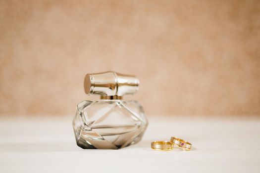 Perfume bottle and gold wedding rings of the bride and groom on a light background. High quality photo
