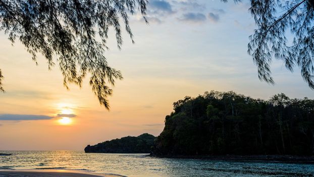 Beautiful nature landscape of colorful the sun on the sky at Tarutao island beach during the sunset over the Andaman Sea under the tree shadow, Tarutao National Park, Satun, Thailand