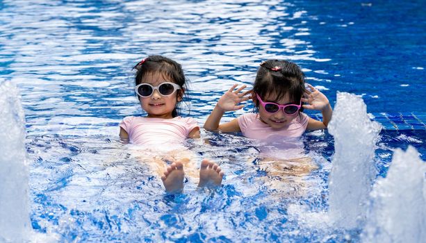 Portrait of pretty asian twins smilling and posing on swimming pool background wearing pink swim suit and sun glasses