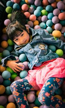 Little Asian girl in a ball pit smiling at the camera, having fun at the children play center