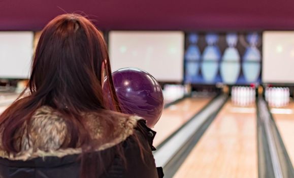 A bowling ball while being aimed to the target by a female adult in a bowling tournament. Purple  bowling ball and blurry bowling alley background