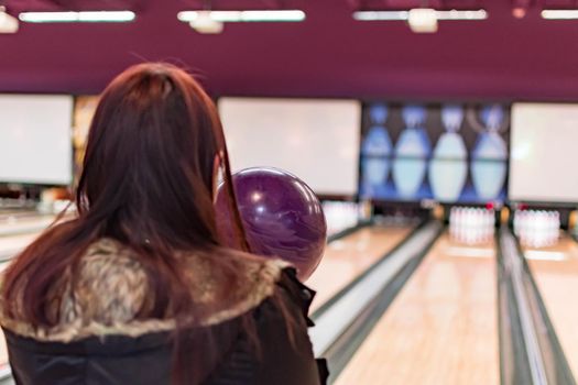 A bowling ball while being aimed to the target by a female adult in a bowling tournament. Purple  bowling ball and blurry bowling alley background