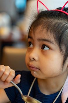 Female asian child while eating rice using spoon. Child enjoys eating rice by her own. Child learning to use spoon and eat by her own