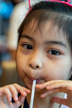 Asian child cute or kid girl drinking water or soy milk beverage in bottle by tube or straw and eating snack or dessert