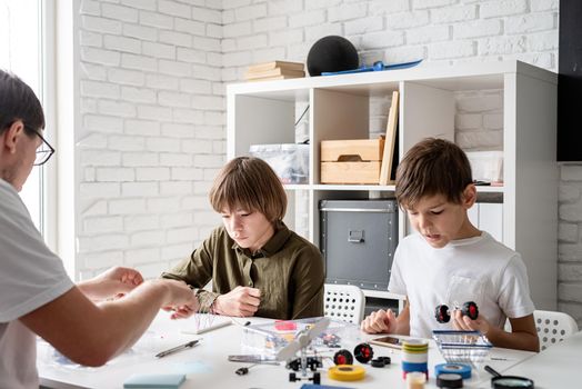 Young boys and teacher having fun constructing robot cars together at the workshop