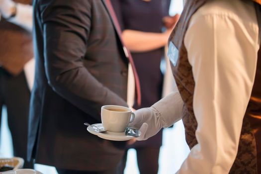 Waiter's hands with a cup on the background of a man