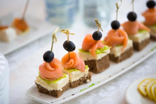 Buffet dishes.Canapes on a white plate. Small sandwiches on a stick. Snack of black bread, salmon and salad