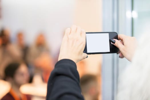 Hands holding smartphone with empty screen en against blurred people background.