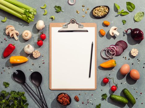Food ingredients, salad serving utensils and clipboard with white paper sheet. Various of vegetarian cooking ingredients on gray background. Diet menu concept. Copy space for text. Top view, flat lay
