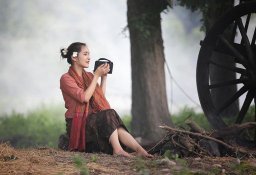 Asian woman wearing traditional thai culture, in field, vintage style listening radio on buffalo and farm background