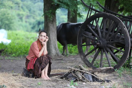 Thai woman farmer wearing local thai tradition sitting on her farm and buffalo  background,countryside Thailand