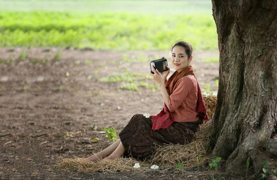Asian woman wearing traditional thai culture, in field, vintage style listening radio on buffalo and farm background
