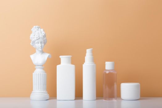 Set of cosmetic products with gypsum figure on white table against beige background. White unbranded cosmetic tubes in a row. Concept of skin care and beauty