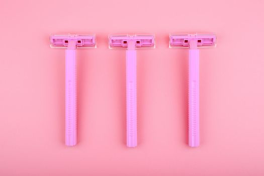 Top view of three pink razors in a row against pink background. Concept of smooth skin, shaving and epilation