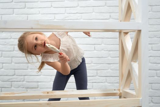 Close up of child smiling and painting with brush wooden rack in white color. Concept of repair at home.