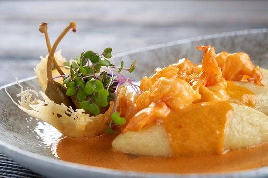 Closeup of shrimps cooked in restaurant for dinner. Delicious exotic seafood with orange sauce on plate on table, three potato cutlets served with vegetables and berries. Concept of food and cuisine.