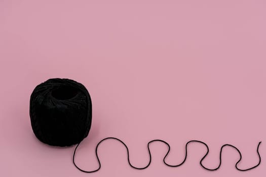 A ball of black braided small robe, made from synthetic yarn, for tying up something, for pink background.