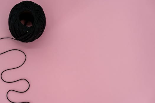 Black ball thread. A ball of black braided small robe, made from synthetic yarn, for tying up something, for pink background.