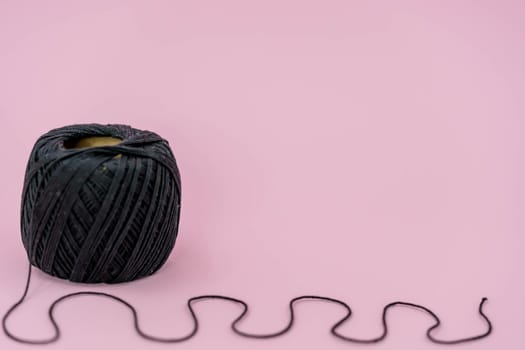 Black ball thread. A ball of black braided small robe, made from synthetic yarn, for tying up something, for pink background.