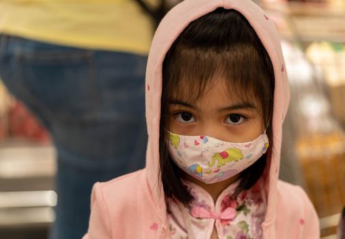 Little girl with fabric mask protect herself from Coronavirus when child go to supermarket. Little asian girl wearing mask in a market