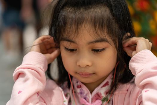 Cute Asian little girl while listening to music wearing earphone