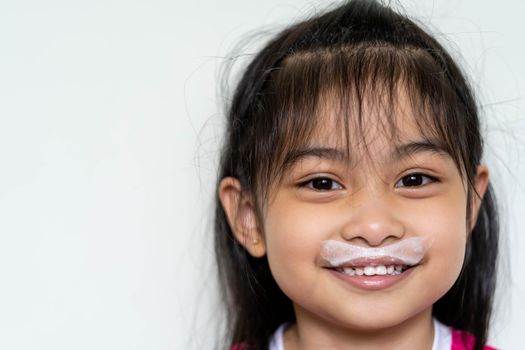 Close up fun portrait of cute Asian girl showing white milk mustache.Isolated against light background.