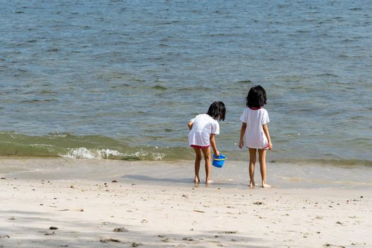 two little girls sitting by the edge of ocean on a sandy beach