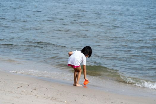 Back of a cute little girl playing with sand and water on a beach