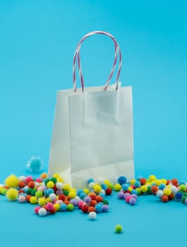 White shopping bagds on blue background. Closeup shot of colorful shopping bags with colorful pom pom balls