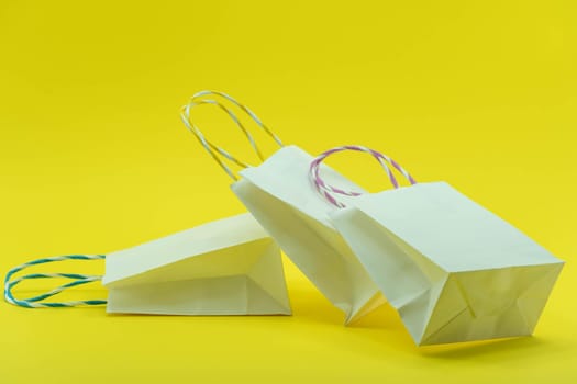 Colourful paper shopping bags isolated on Yellow Background. Closeup shot of white shopping bags