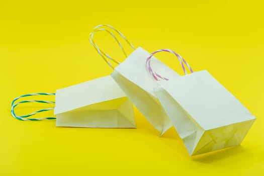 Colourful paper shopping bags isolated on Yellow Background. Closeup shot of white shopping bags