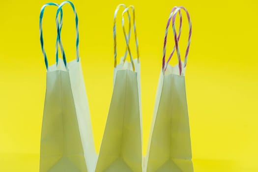 Colourful paper shopping bags isolated on Yellow Background. Closeup shot of white shopping bags