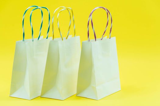 Colourful paper shopping bags isolated on Yellow Background. Closeup shot of white shopping bags