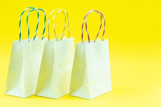 Colourful paper shopping bags isolated on Yellow Background. Closeup shot of white shopping bags