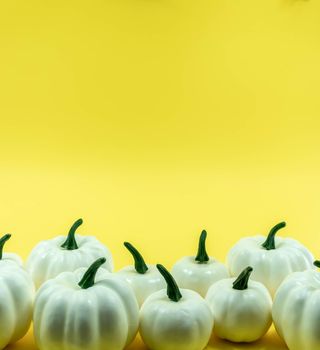 Autumn bottom border banner of white pumpkins, gourds and fall decor on yellow background with copy space