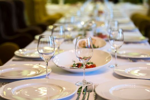 Served table in a restaurant. Plates glasses cutlery on a long table.