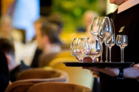 Hands hold a tray with glasses. Waiter on the background of the restaurant.