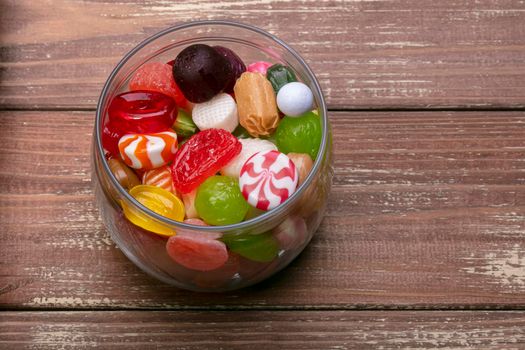 Candies in a jar on a wooden background. Multi-colored caramel. Sweets.