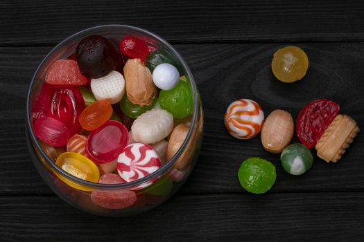 Candies in a jar on a dark background. Multi-colored caramel on a wooden board. Sweets.