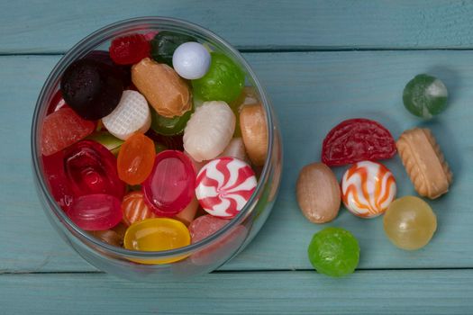 Candies in a jar on a blue background. Multi-colored caramel on a wooden board. Sweets.
