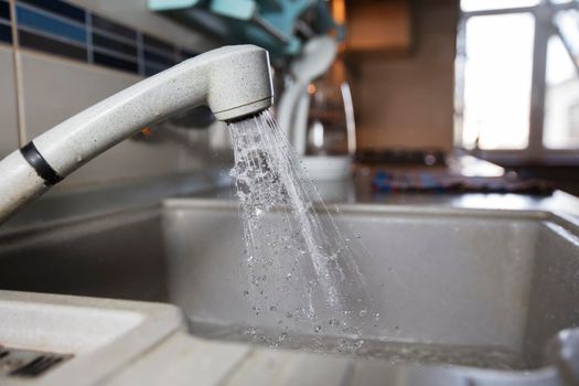 Water is pouring from a faucet. Water tap on the background of the kitchen. House water consumption.