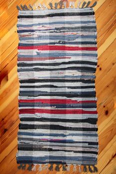 Rustic wicker rug on a wooden floor. Multi-colored Slavic carpet.